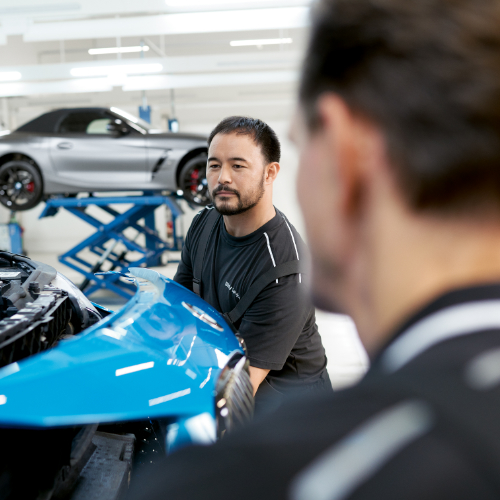 Two BMW Trained Technicians attach a front bumper on a BMW vehicle in a BMW Certified Collision Repair Center.