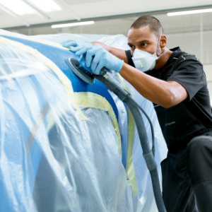 BMW Trained Technician wearing protective gear performs paint work on a BMW vehicle in a BMW Certified Collision Repair Center.