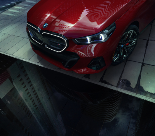 Three quarter, overhead view of a hood, grille, wheel and tire from a parked, red BMW i5 M60.